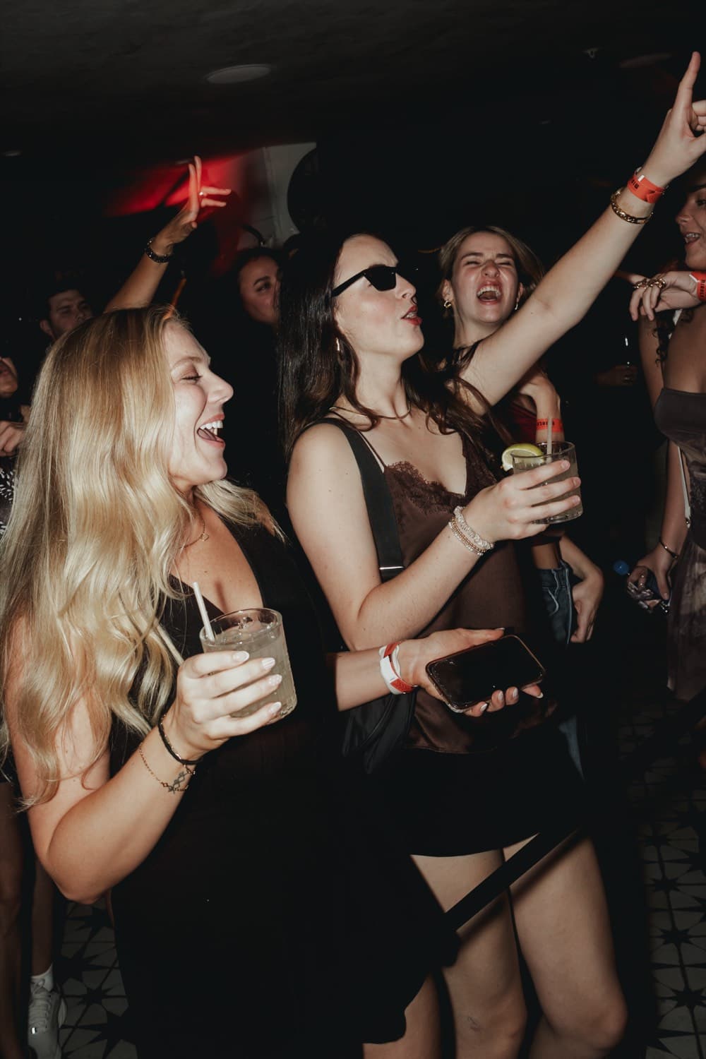 A woman dancing with her arm raised, drink in hand, under red light