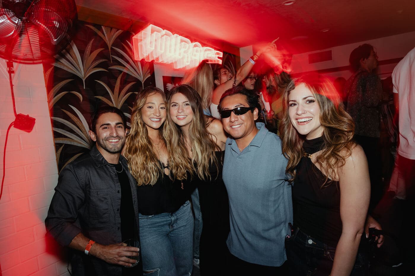 A group of five posed together in front of the glowing Mirage sign