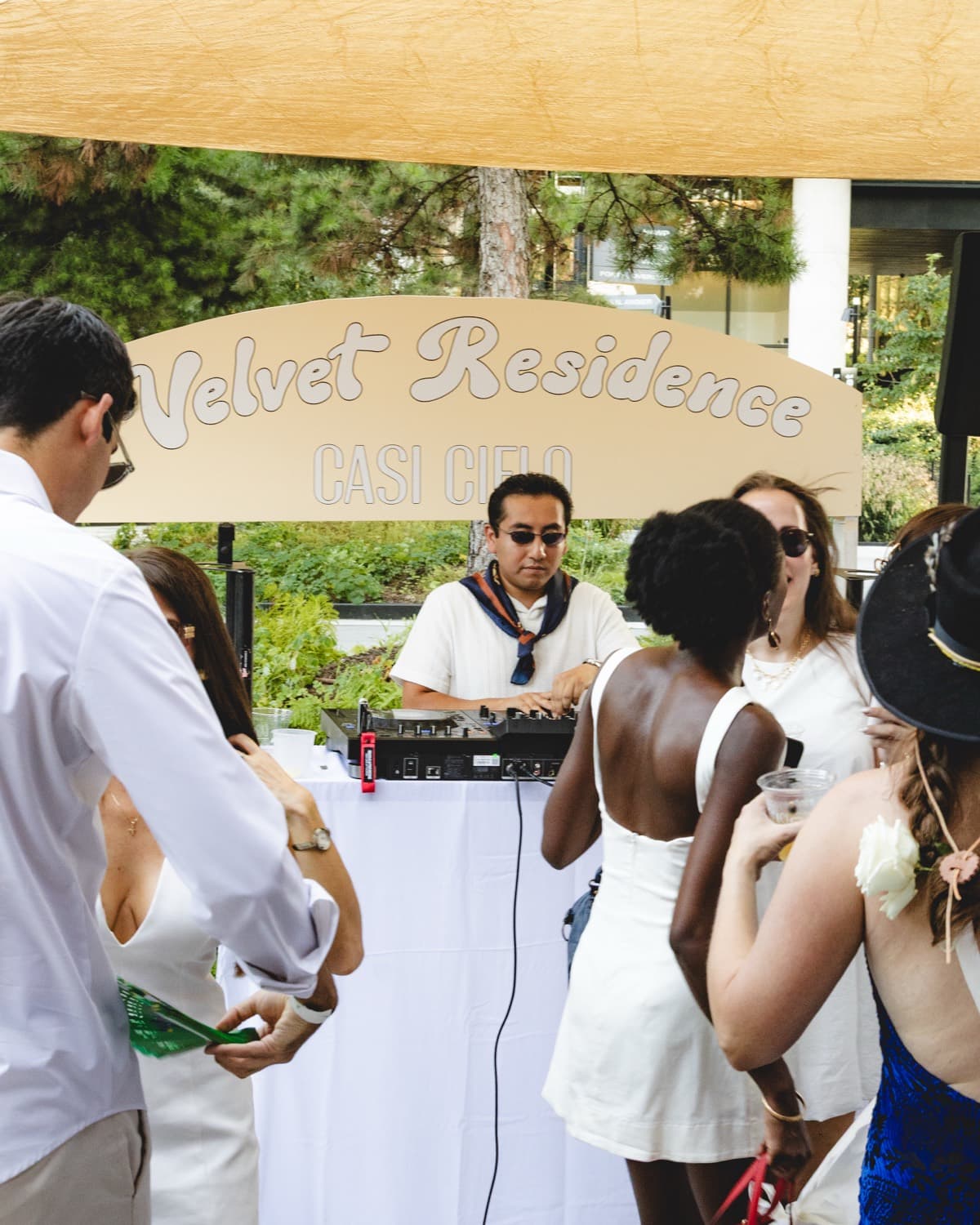 LP DJing outdoors in a white polo and sunglasses under the Velvet Residence sign